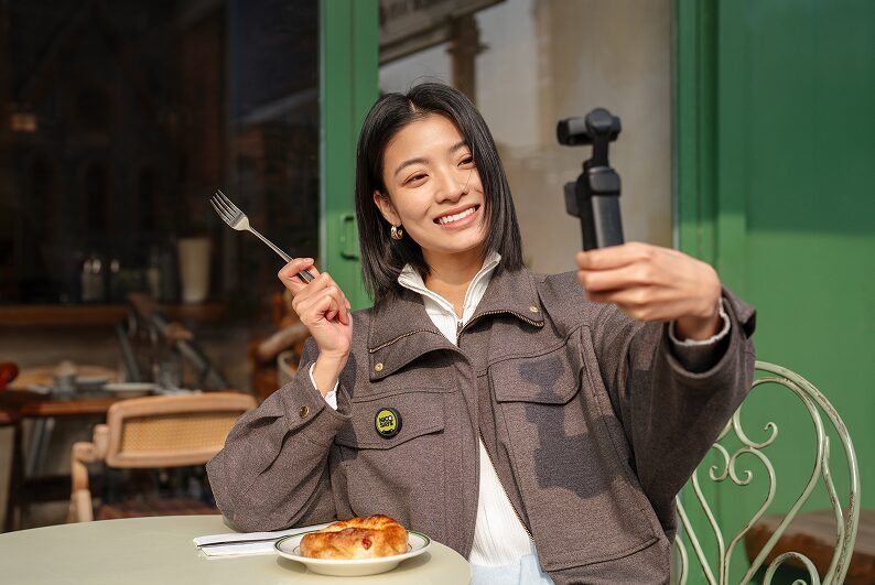 Insta360 Micの送信機を胸元に着け、手持ちのInsta360カメラでカフェの食事を自撮りする女性