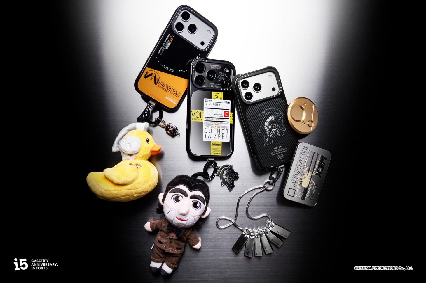 KOJIMA PRODUCTIONS x CASETiFYのスマホケース、アヒルーデンスとドールマンのぬいぐるみキーホルダー、メタル製グリップスタンドなどを並べたコレクション画像