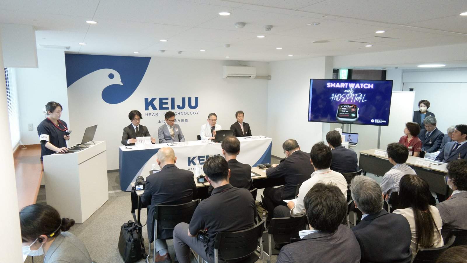恵寿総合病院の記者会見の会場。KEIJUのロゴの前に登壇者が並び、記者が説明を聞いている