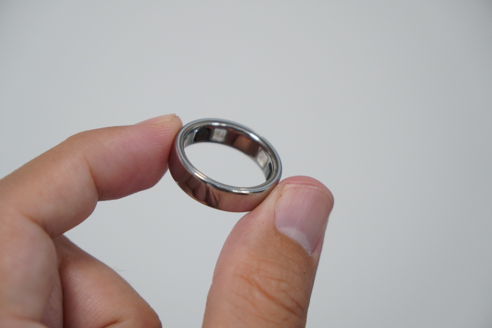 指でつまんだOura Ring 5。鏡面のシルバーで、内側にセンサーの窓が見える