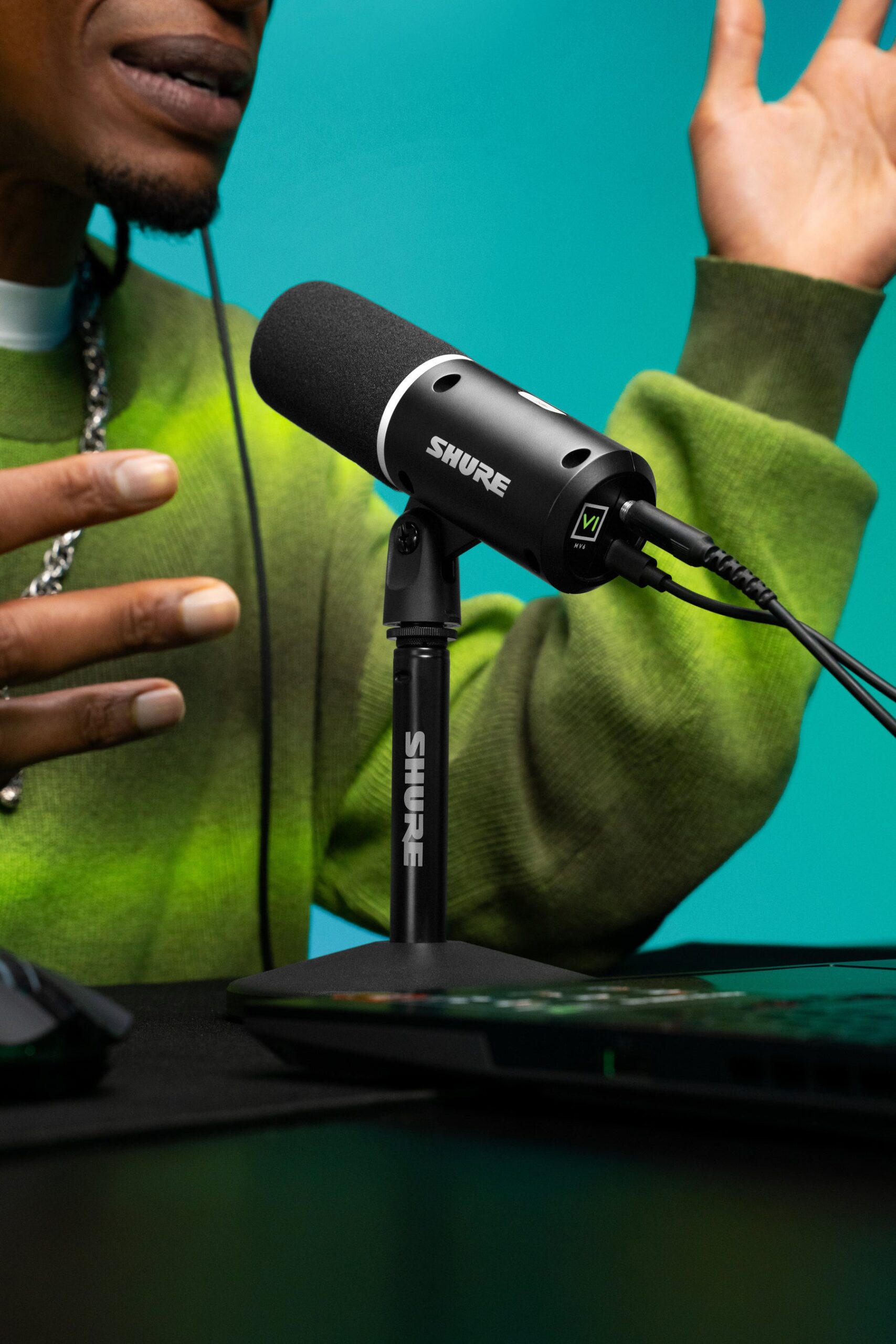 Shure MV6 Gen 2のブラックモデルに向かって身ぶりを交えて話す配信者。デスクトップスタンドに立てたマイクにUSB-Cケーブルとヘッドホンをつないでいる