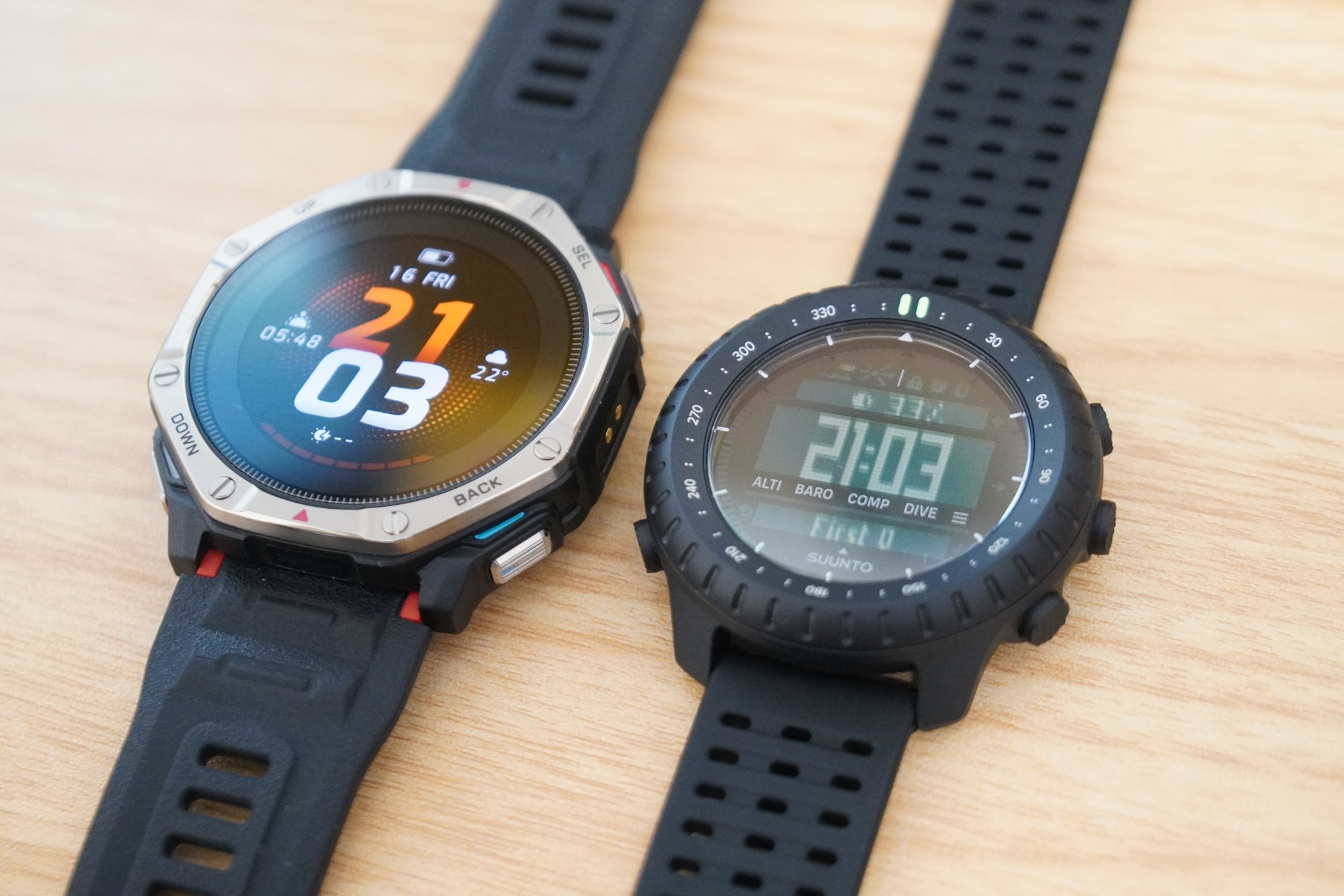 机の上に並べたAmazfit T-Rex Dual Solar(左)とSuunto Core 2(右)。T-Rexはカラーの画面、Core 2は液晶の画面に21時03分と表示されている