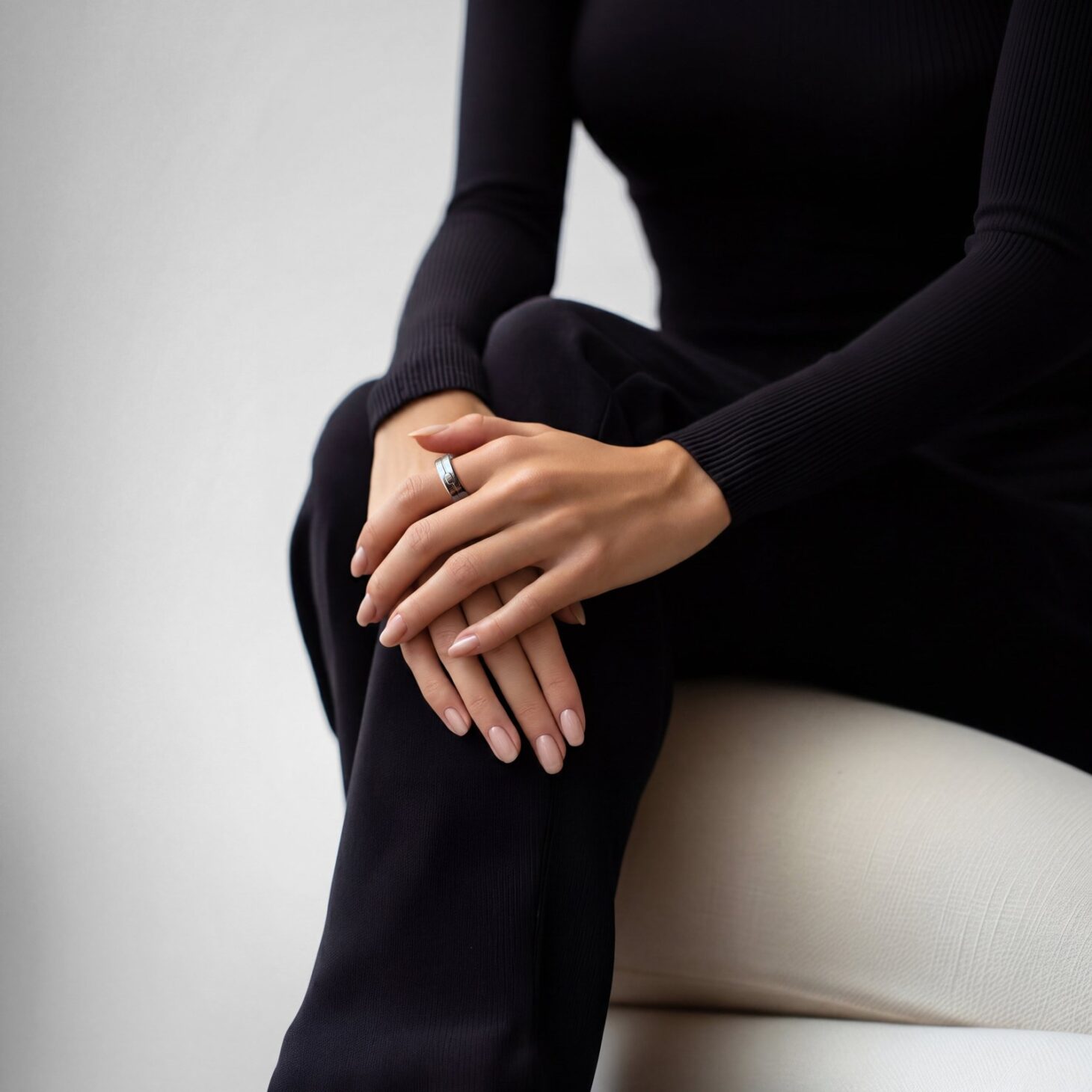 黒い服の女性が指にシルバーの指輪型AI記録デバイス「Vocci」を着け、膝の上で手を重ねている着用イメージ