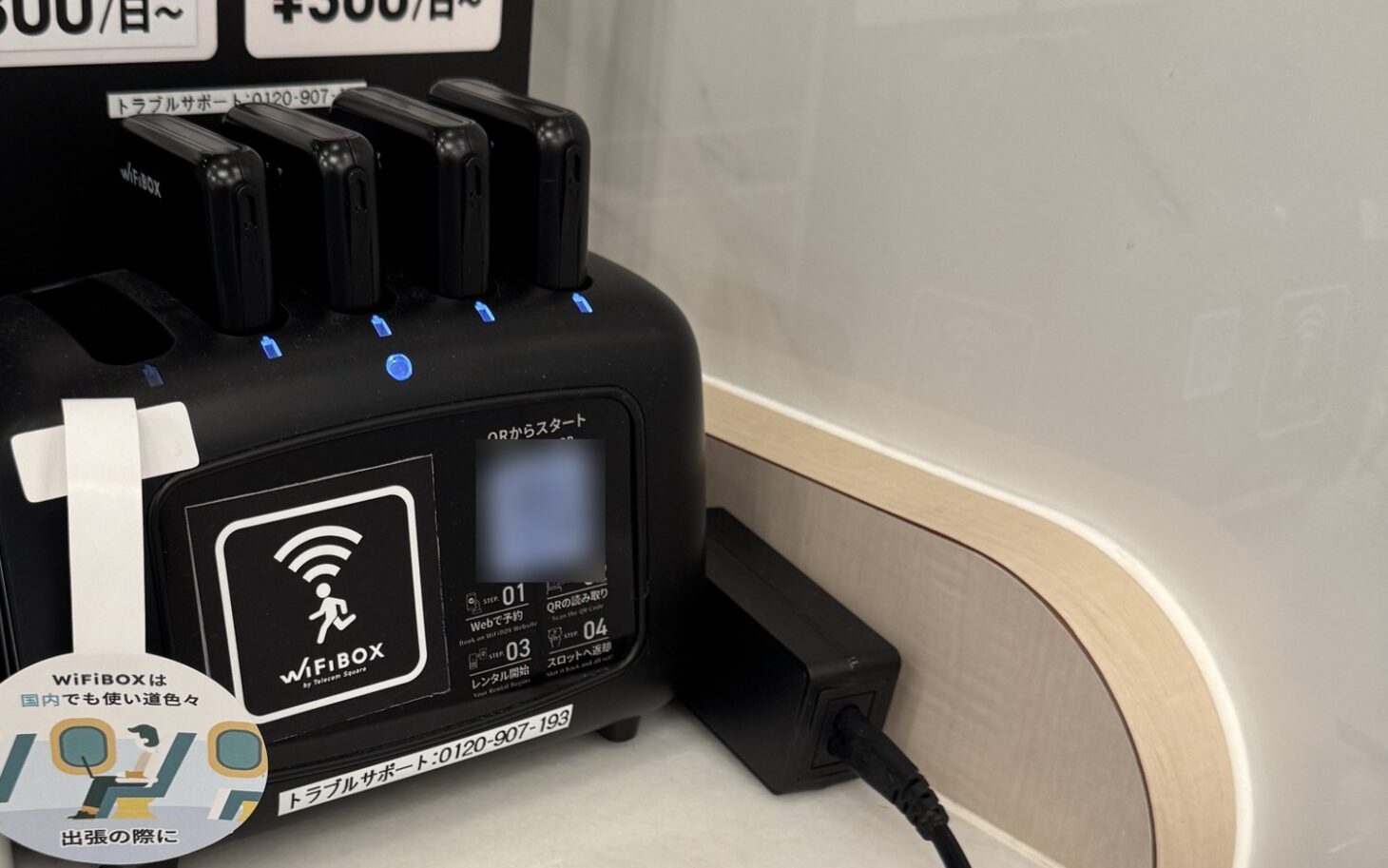 ホテルに設置されたWiFiBOXの貸出機。端末が4台挿さり、本体にWiFiBOXのロゴとQRからスタートの手順が表示されている