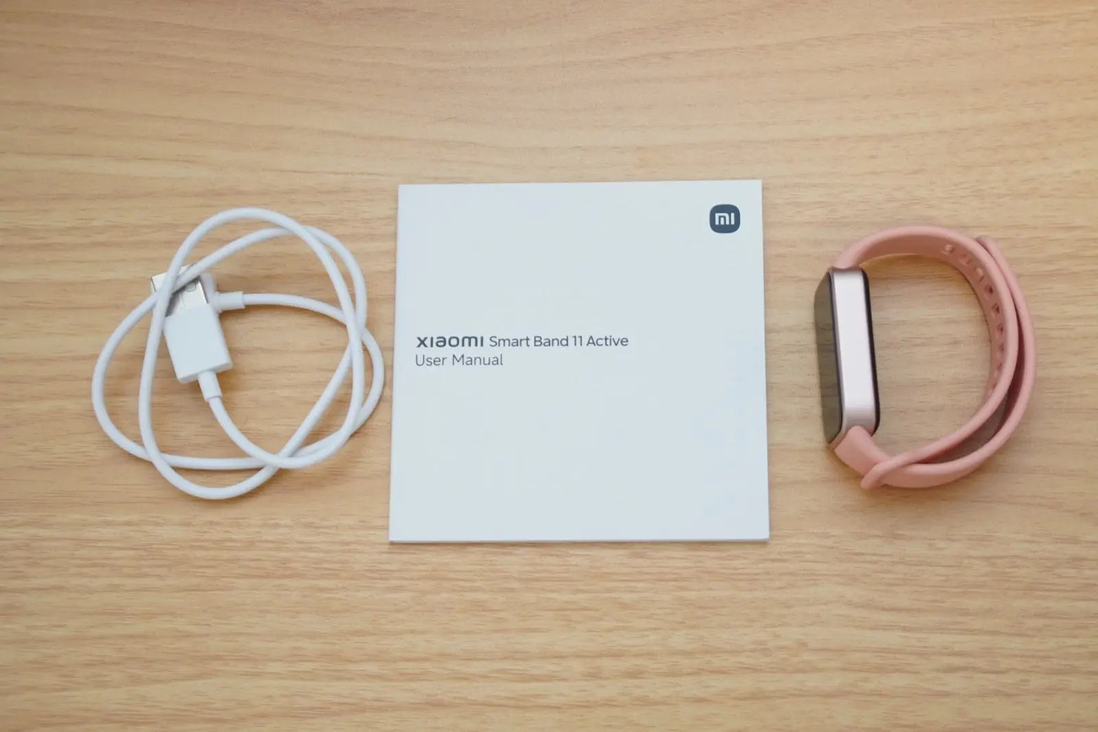 Xiaomi Smart Band 11 Activeの同梱品。白い磁気充電ケーブル、取扱説明書、ピンクのストラップを付けた本体が並んでいる