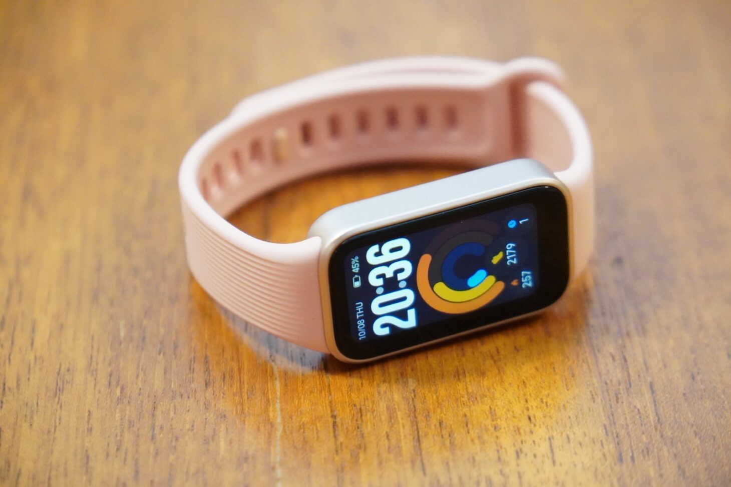 木の机に置いたXiaomi Smart Band 11 Activeのポメロピンク。画面に20時36分とアクティビティのリングが表示されている