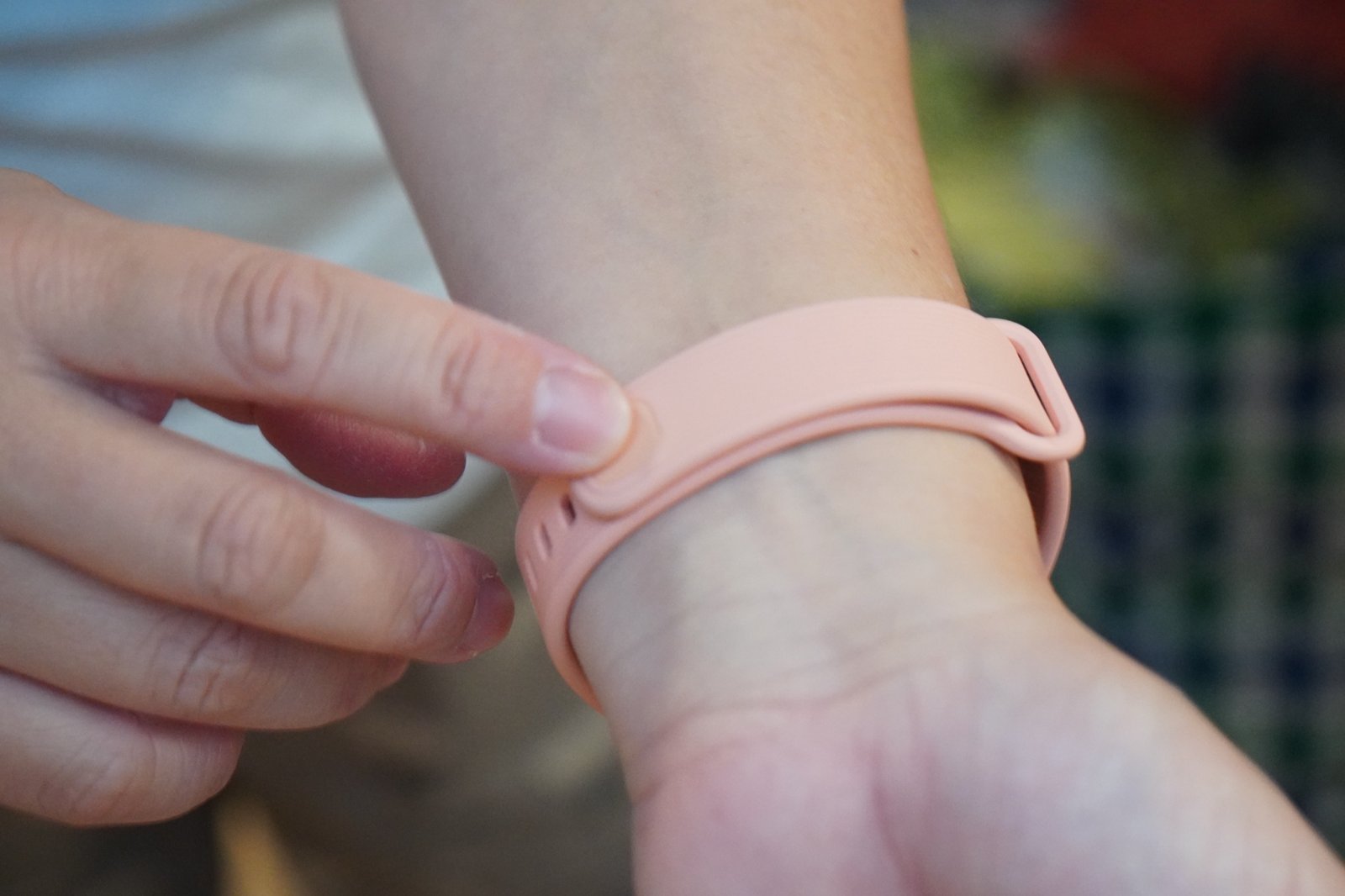 手首に巻いたXiaomi Smart Band 11 Activeのストラップの留め具を指で押し込んでいるところ。留め具もストラップと同じピンクの素材