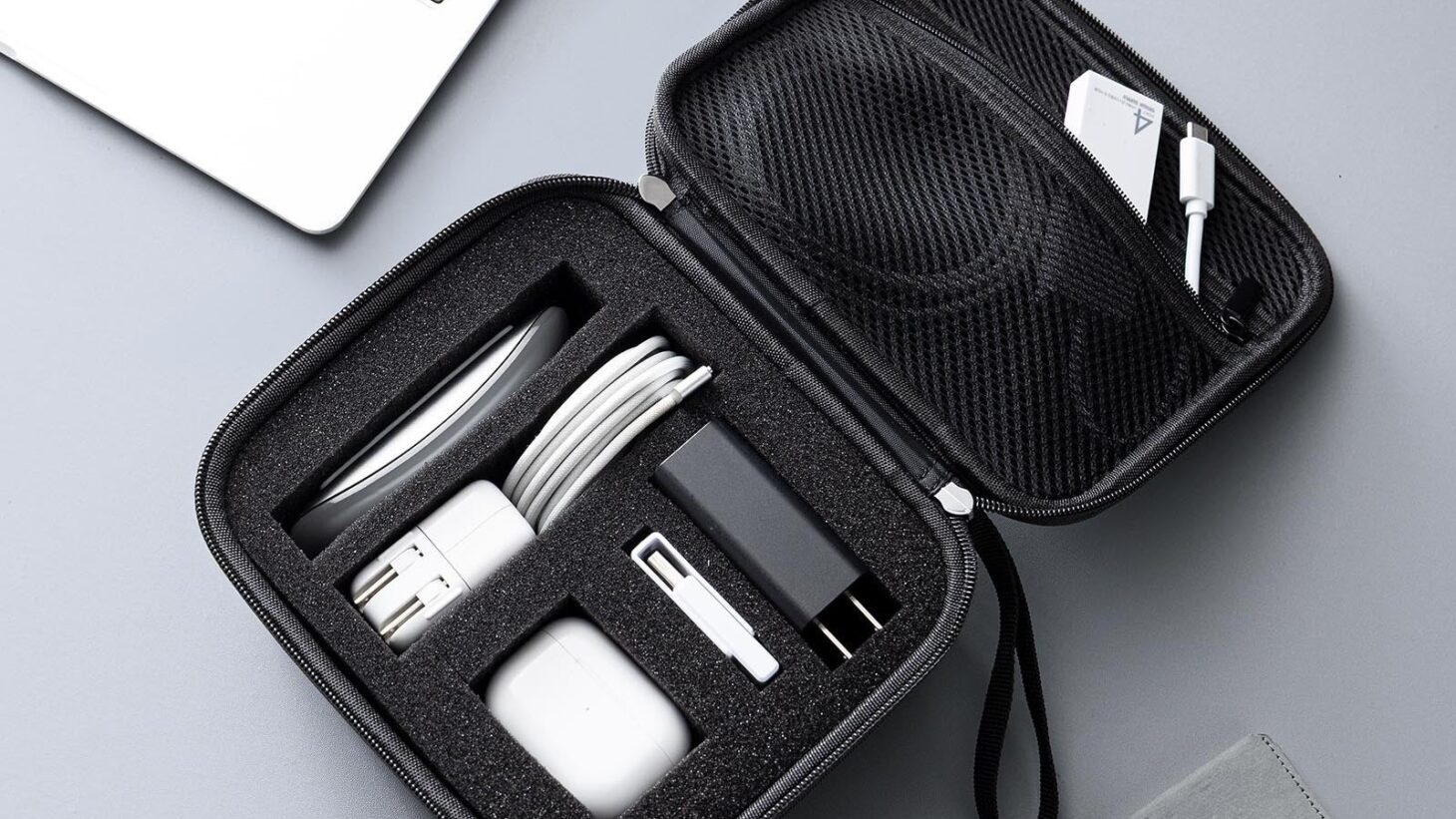 サンワダイレクトのセミハードガジェットポーチMサイズを開き、充電器やケーブル、イヤホンをクッションの区画に収めた様子