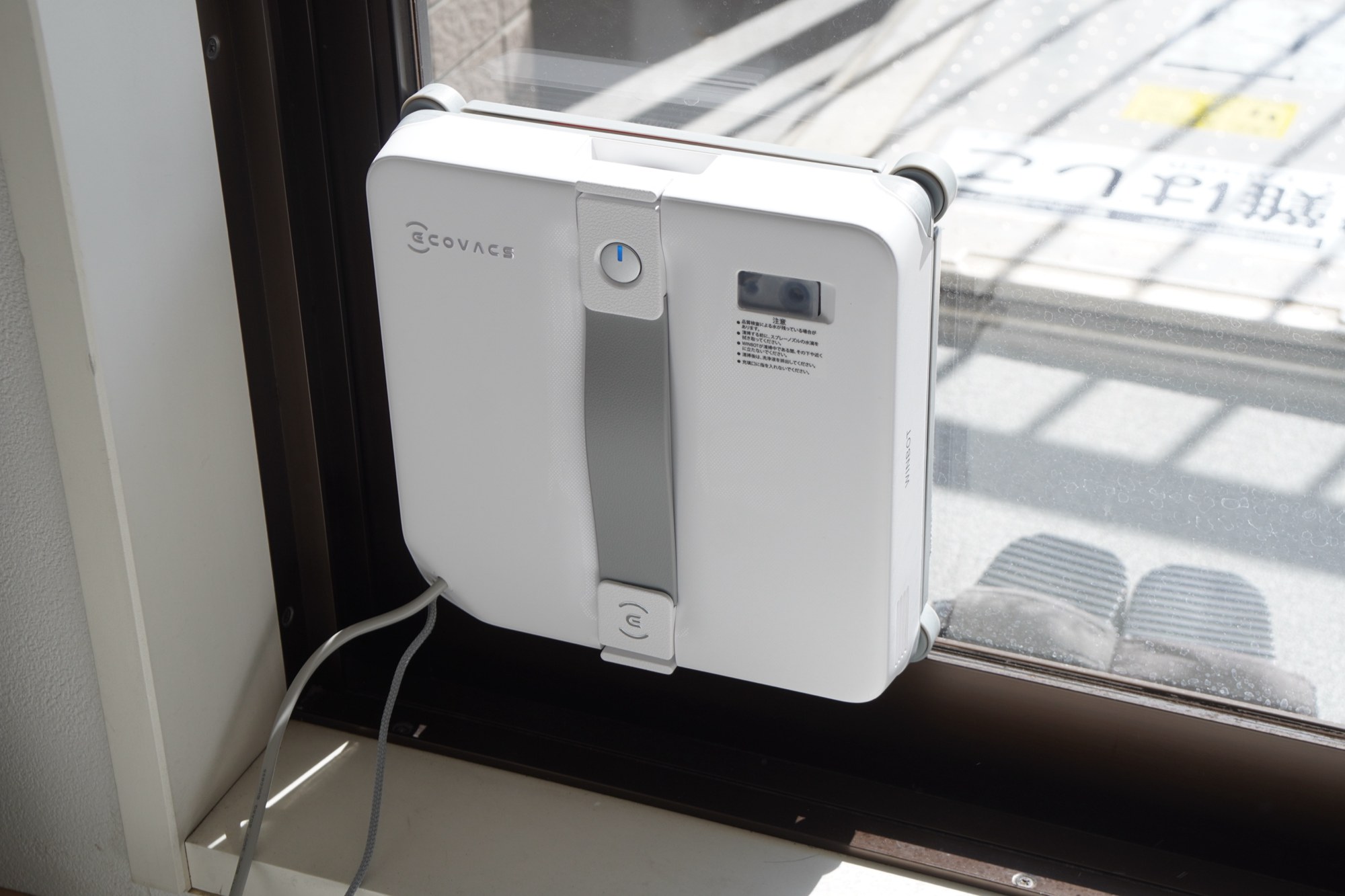 リビングの窓の内側に吸着したWINBOT mini 2。下側から電源ケーブルが出ている
